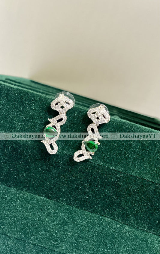 Silver earrings with green gemstones on a green velvet surface
