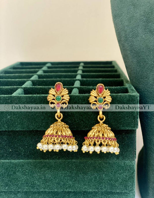 Gold earrings with pearls and gemstones on a green velvet stand.