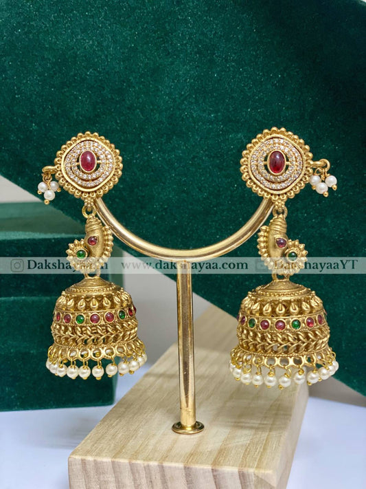 Gold earrings with red and green gemstones on a stand against a green background