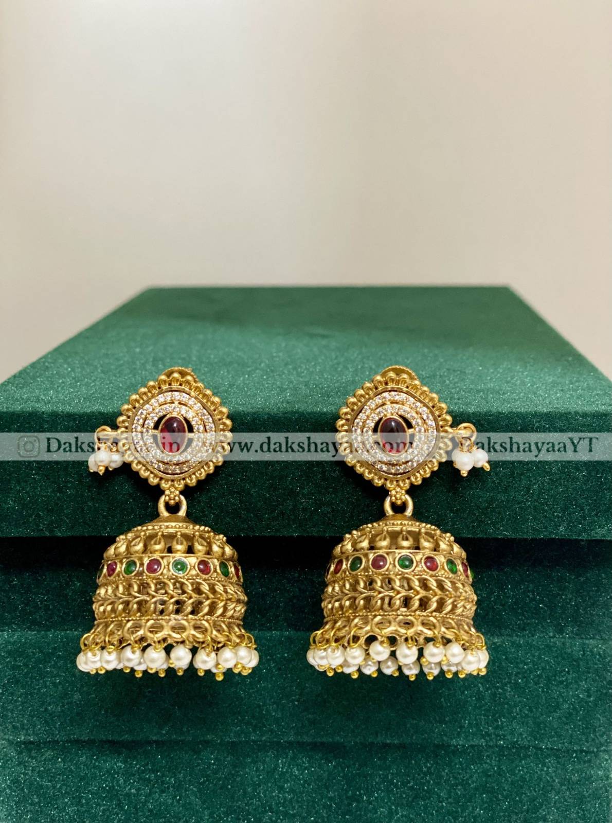 Gold earrings with red and green stones on a green surface