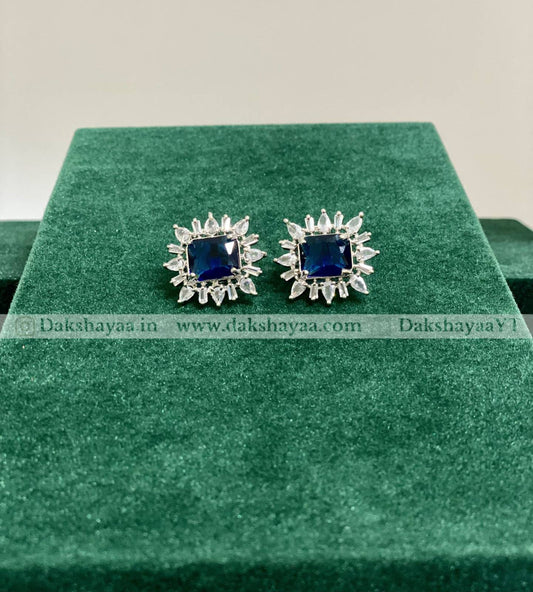 Pair of blue gemstone earrings on a green cushion with 'Dakshayaa' branding.