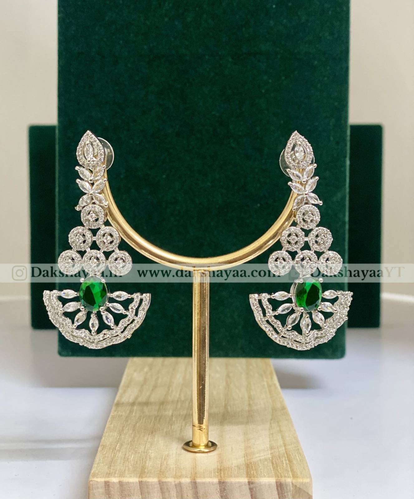 Pair of silver earrings with green gemstones on a gold stand against a green velvet background.