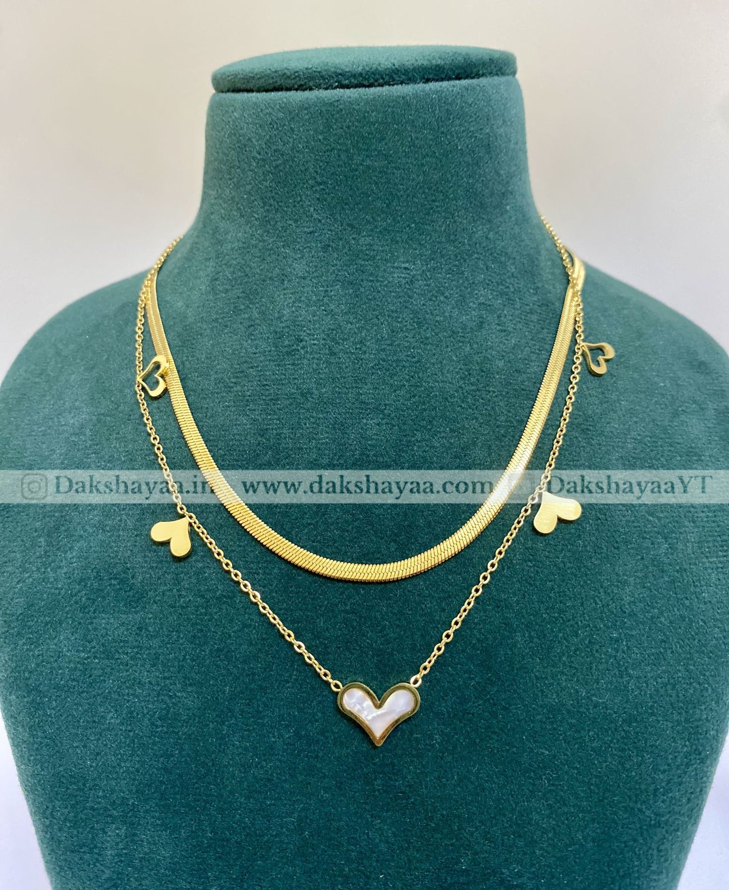 Gold necklace with heart-shaped pendants on a green mannequin bust.