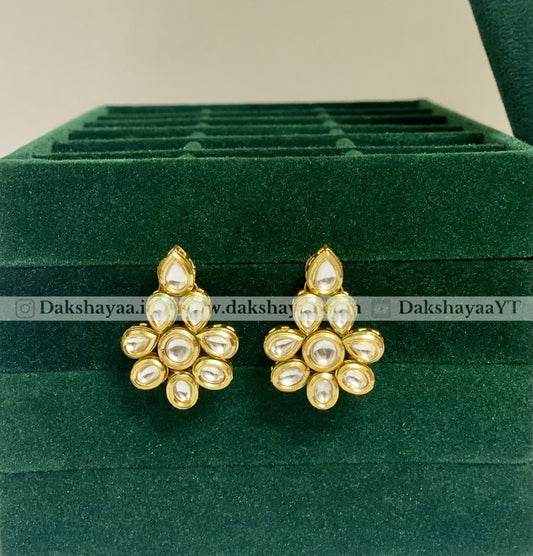 Gold and pearl earrings on a green velvet stand with 'Dakshayaa' branding.