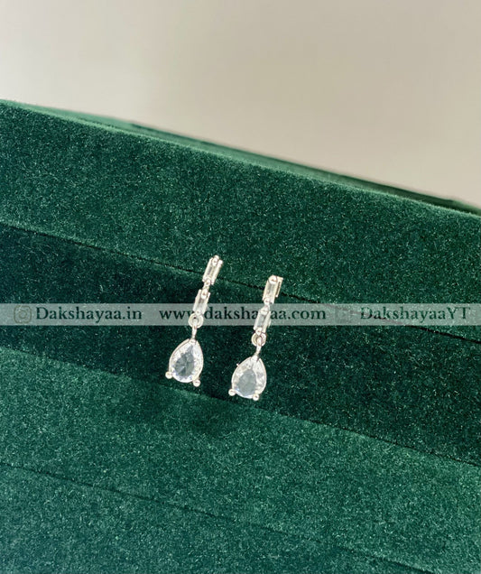 Pair of silver earrings with teardrop-shaped stones on a green velvet surface.