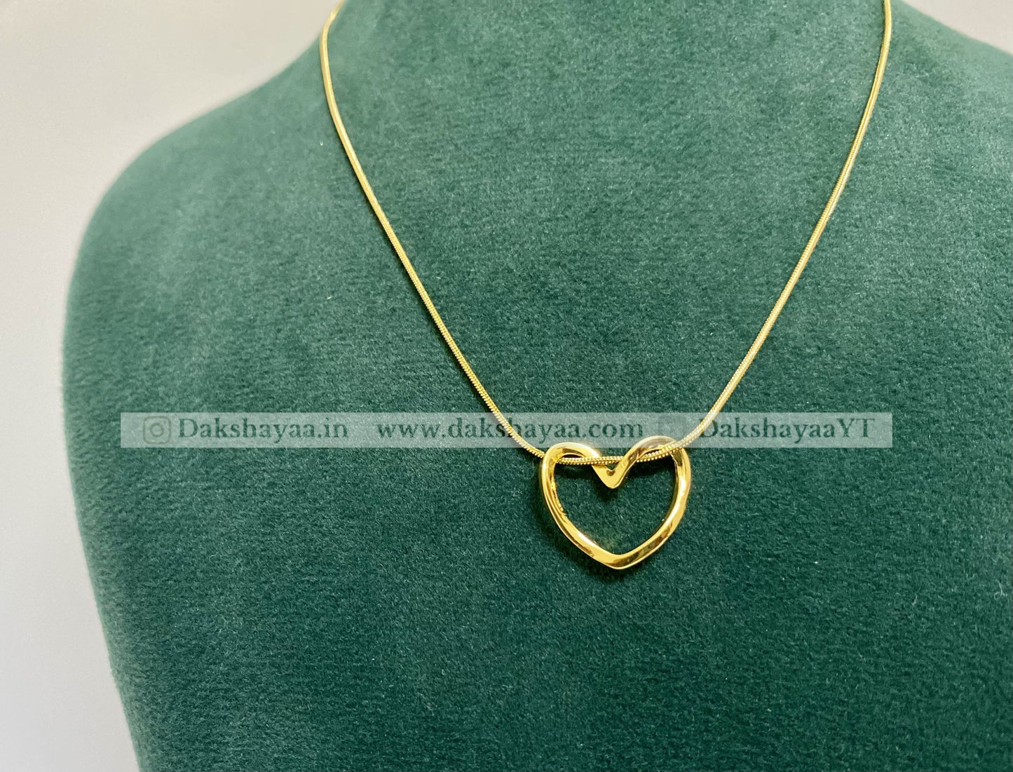 Gold heart-shaped pendant on a green mannequin with visible branding.