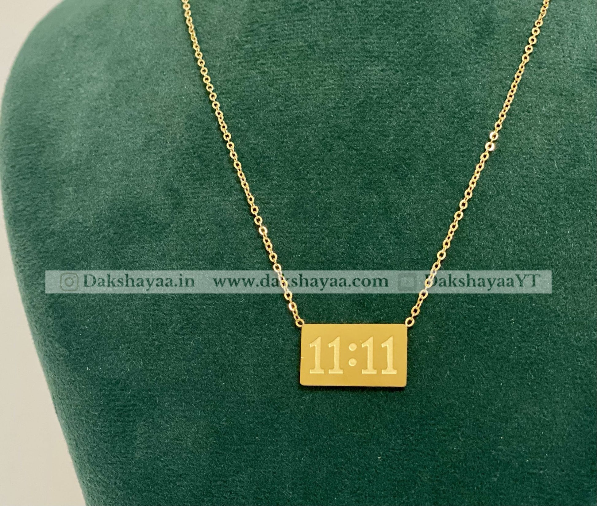 Gold necklace with a square pendant displaying '11:11' on a green cushion.