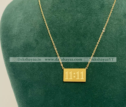 Gold necklace with a square pendant displaying '11:11' on a green cushion.