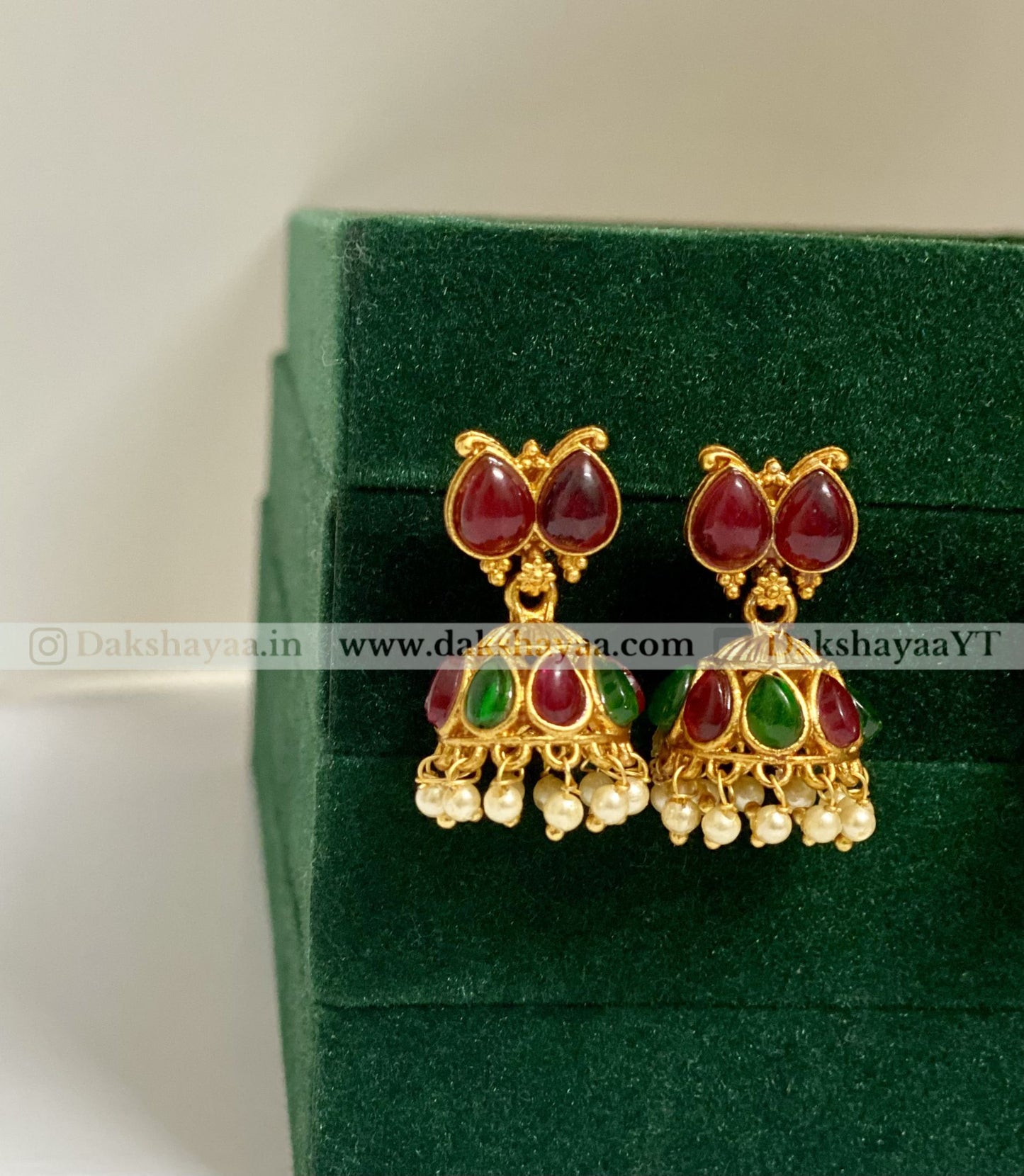 Gold earrings with red and green stones on a green velvet background