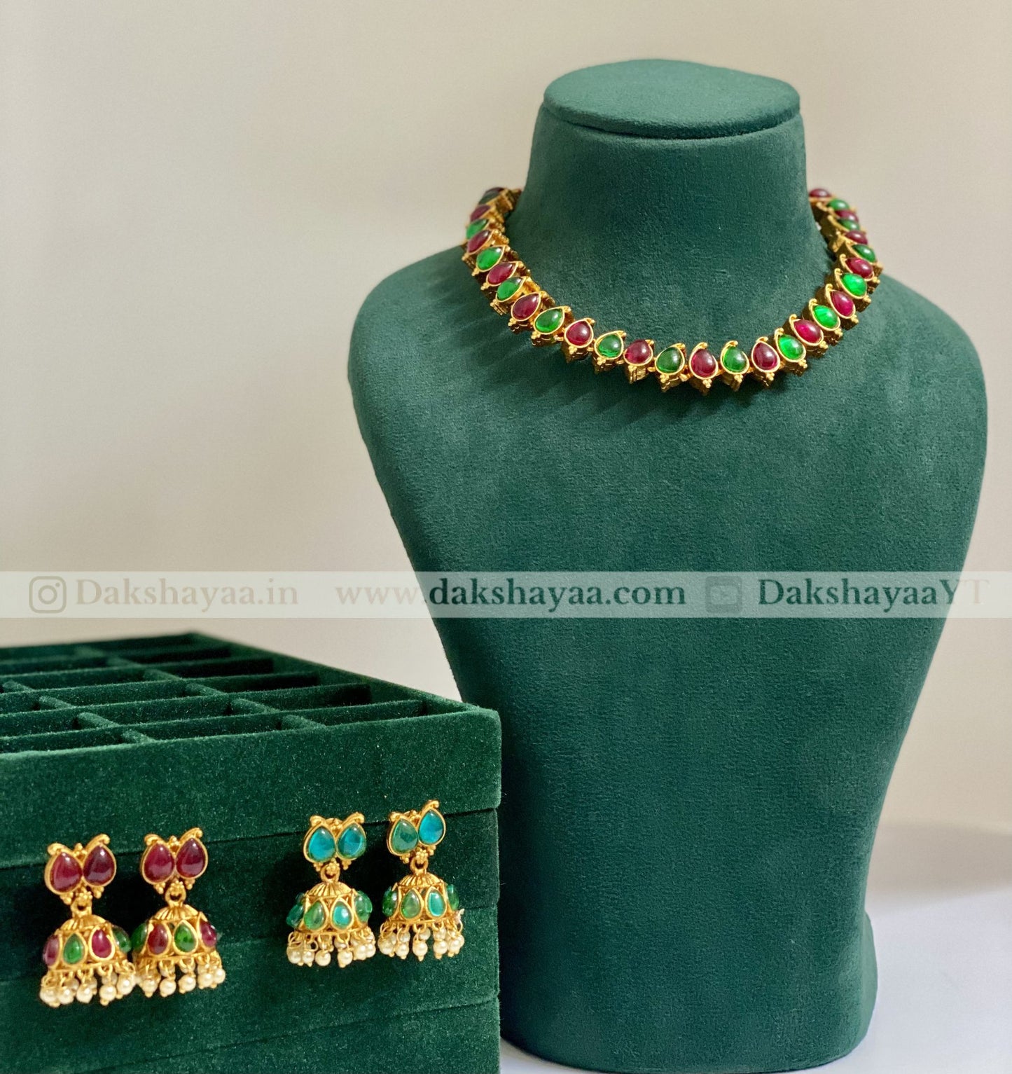 Jewelry set with necklace and earrings on a green mannequin and box, branded 'Dakshayaa'.