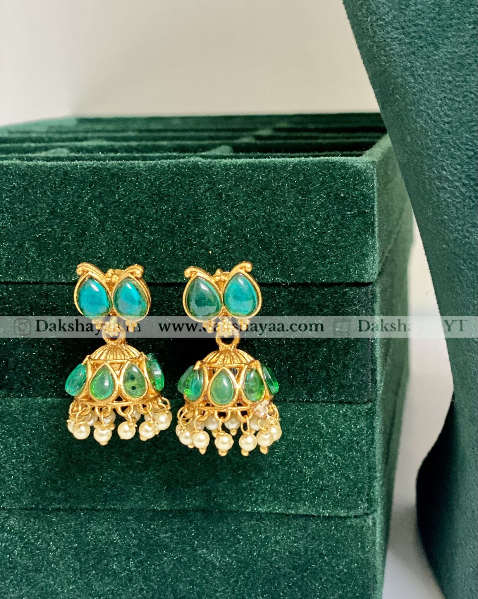 Gold and teal earrings on a velvet stand