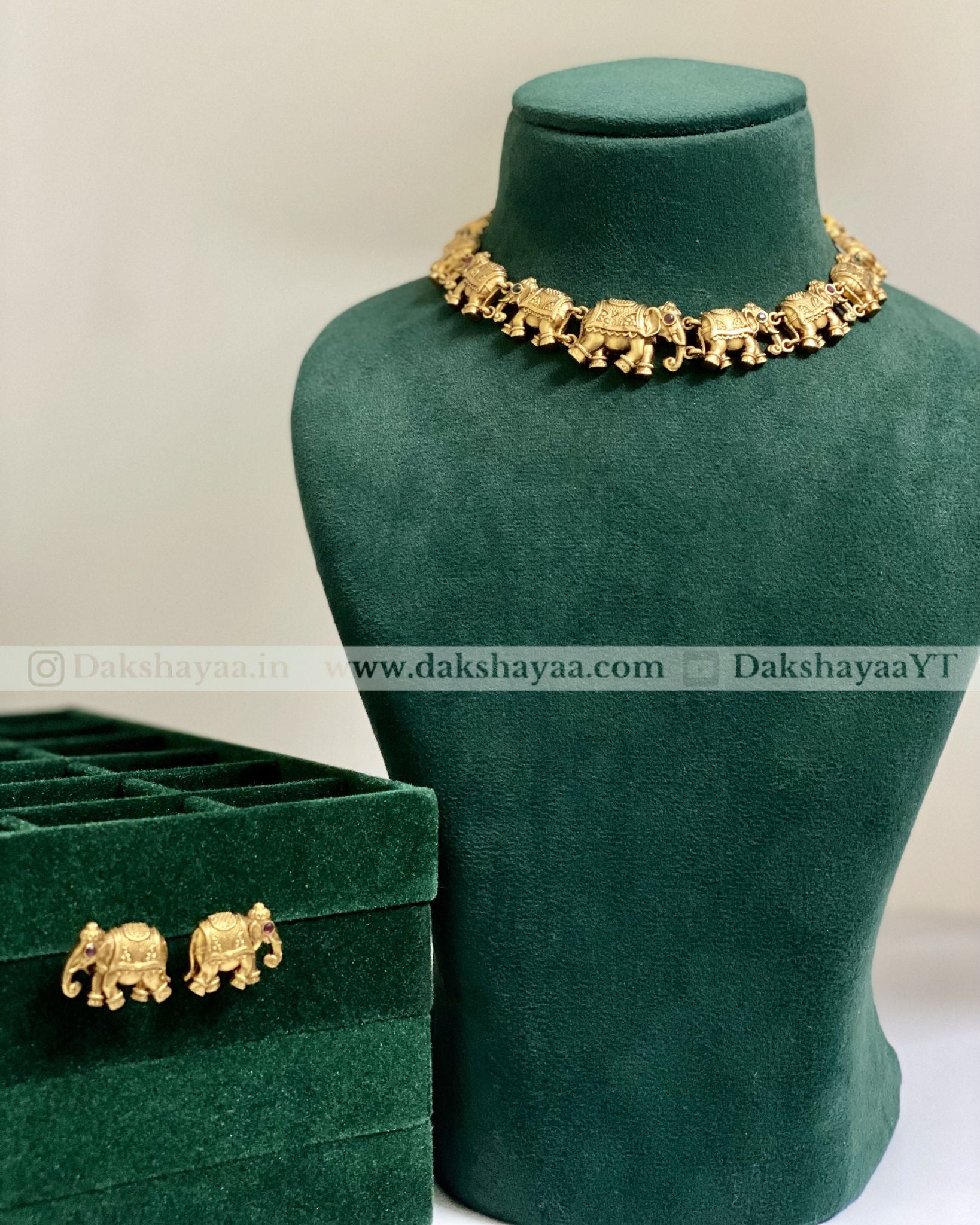 Gold elephant-themed jewelry set on a green velvet stand with a matching box.