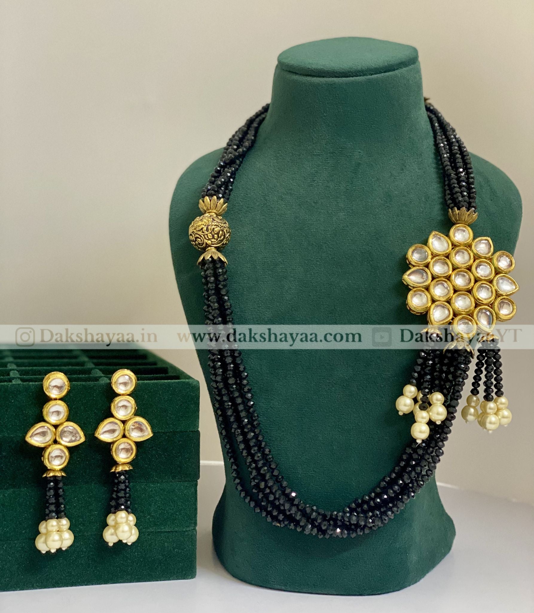 Black beaded necklace with gold and pearl accents on a green mannequin, accompanied by matching earrings on a green stand.