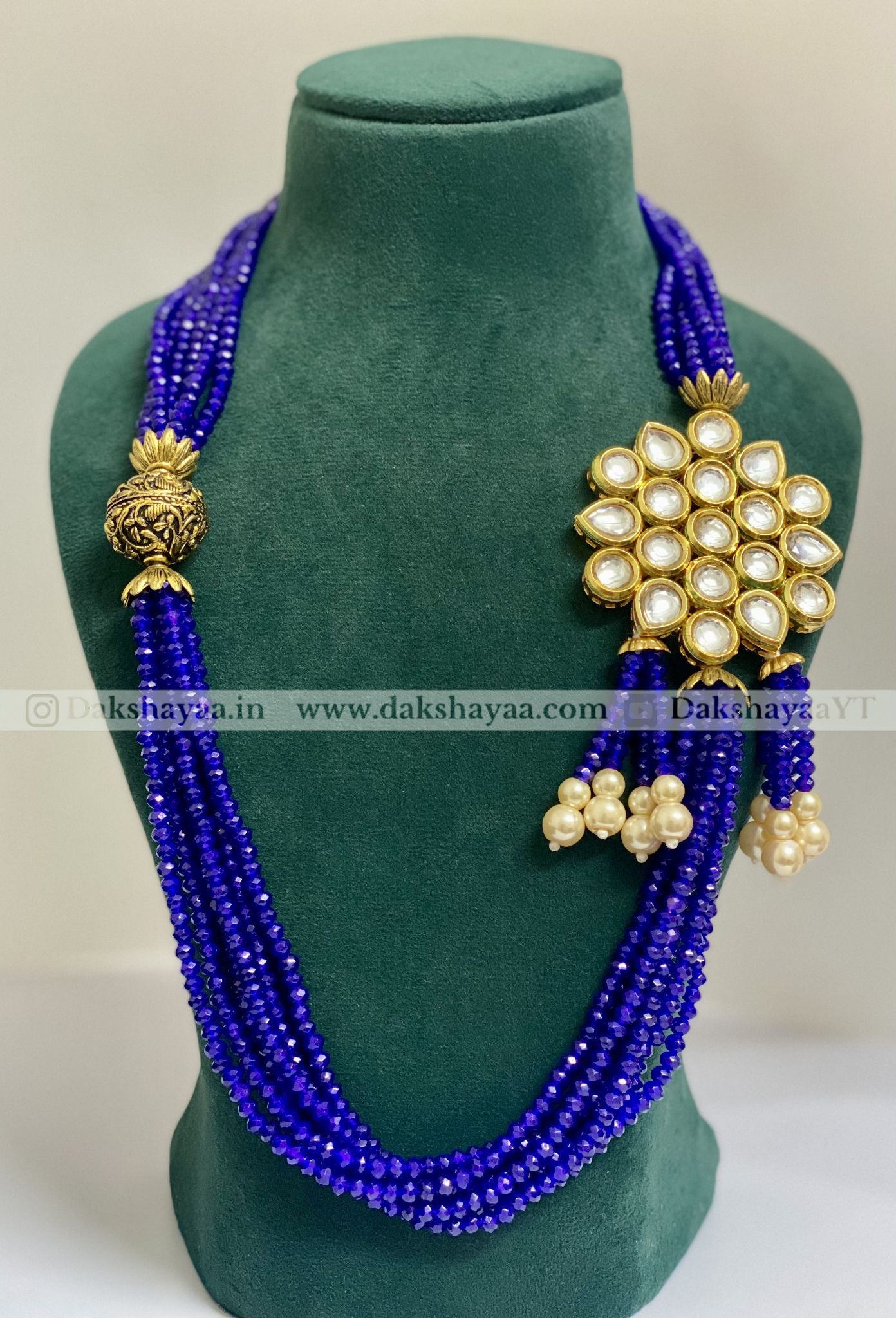 Blue beaded necklace with gold and pearl accents on a green mannequin bust.