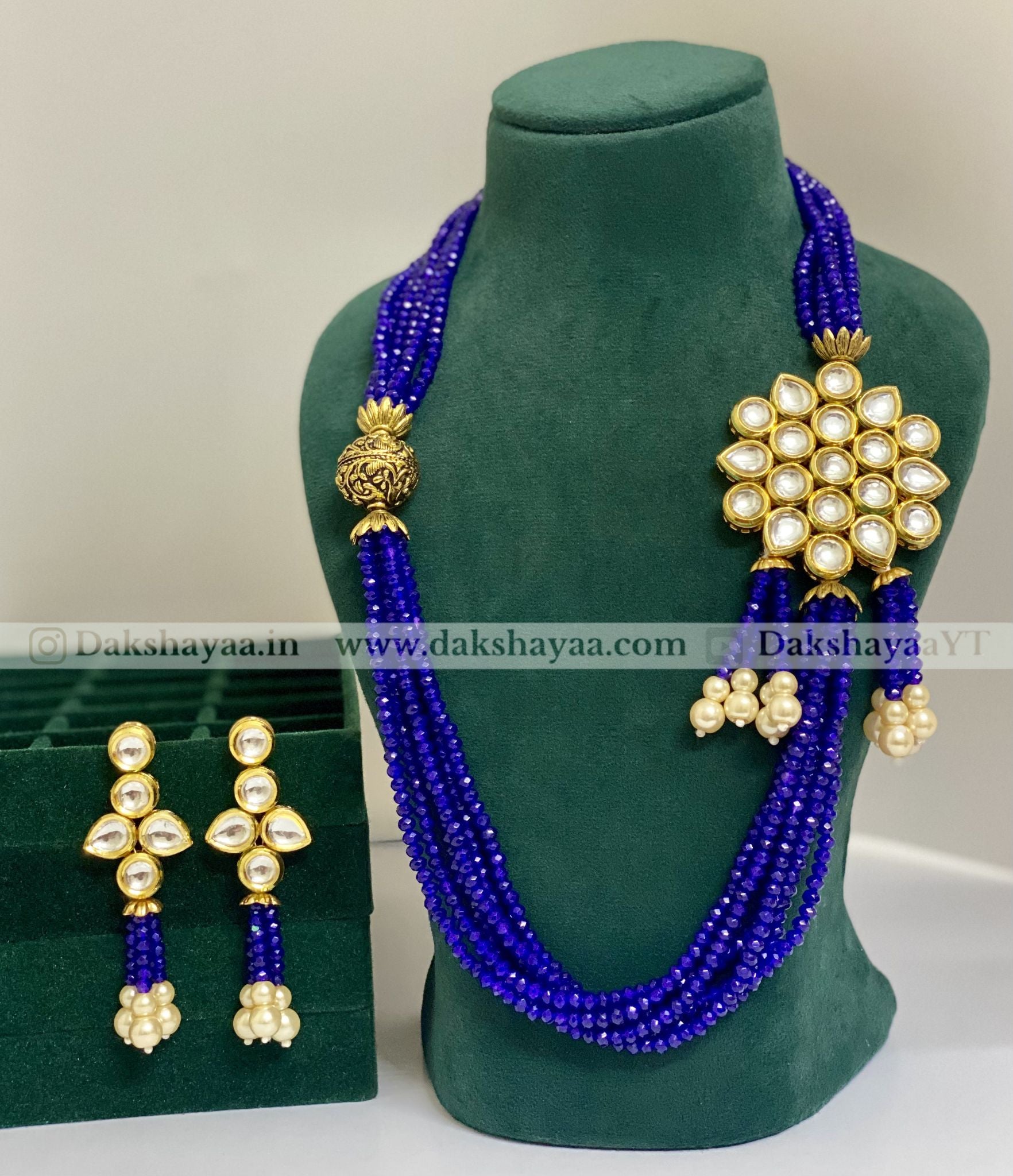 Blue beaded necklace with gold and pearl accessories on a green mannequin.