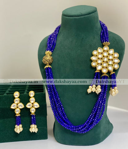 Blue beaded necklace with gold and pearl accessories on a green mannequin.