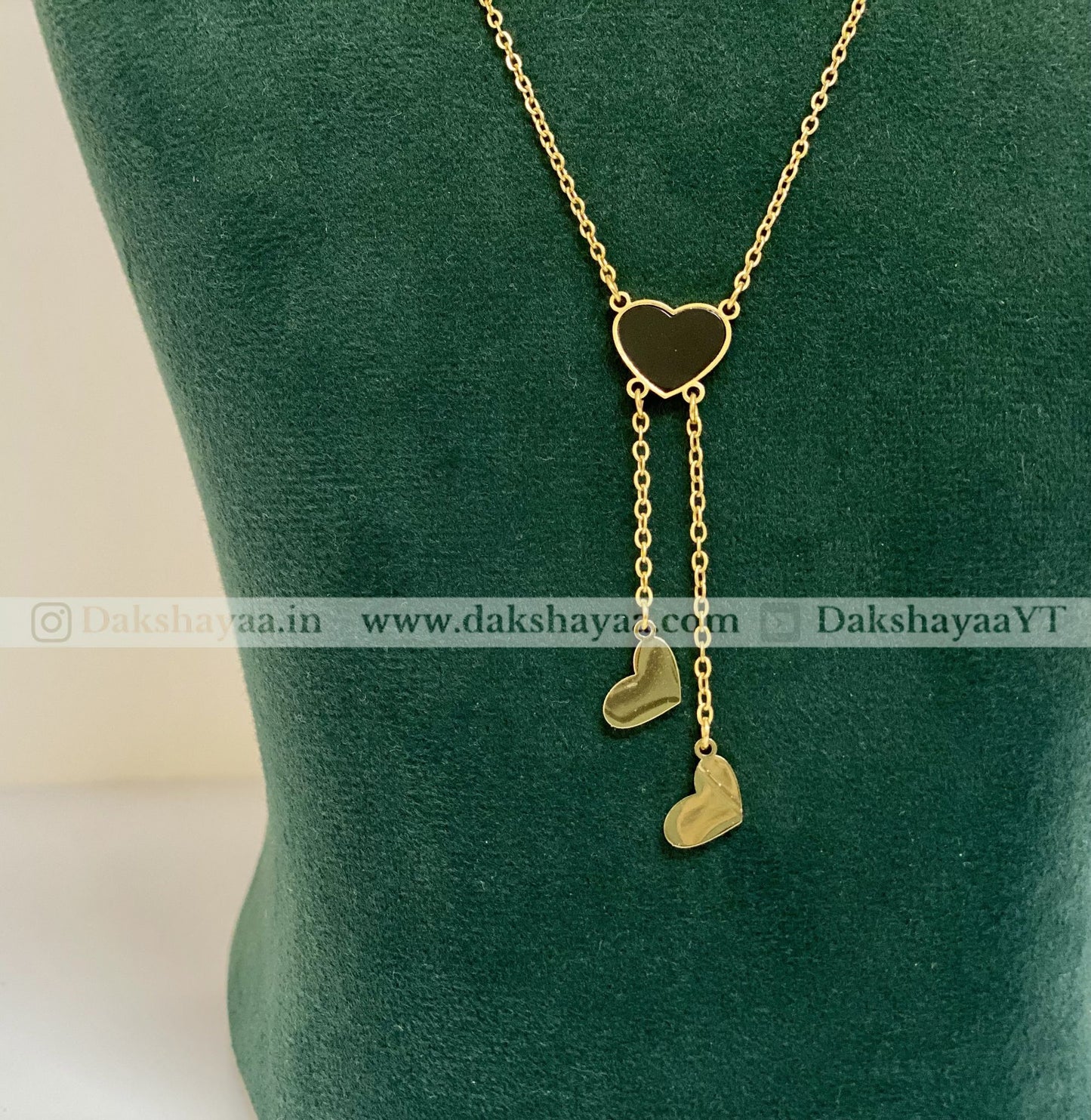 Gold necklace with heart-shaped pendants on a green velvet stand.