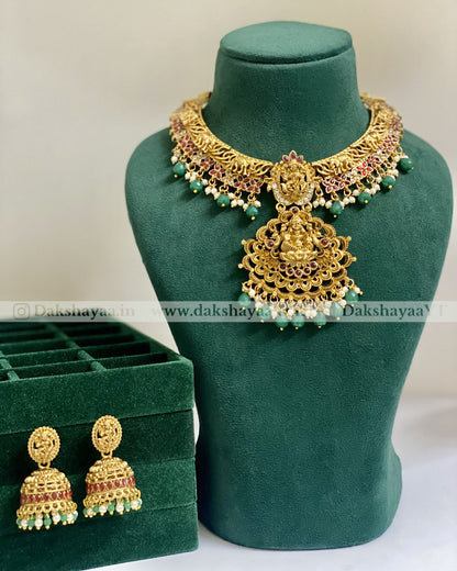 Gold necklace and earrings on a green mannequin with 'Dakshayaa' branding.
