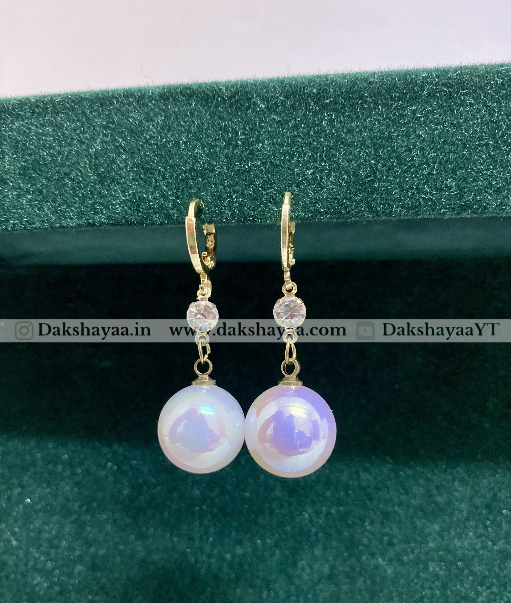 Pearl earrings with gold hooks on a green velvet background