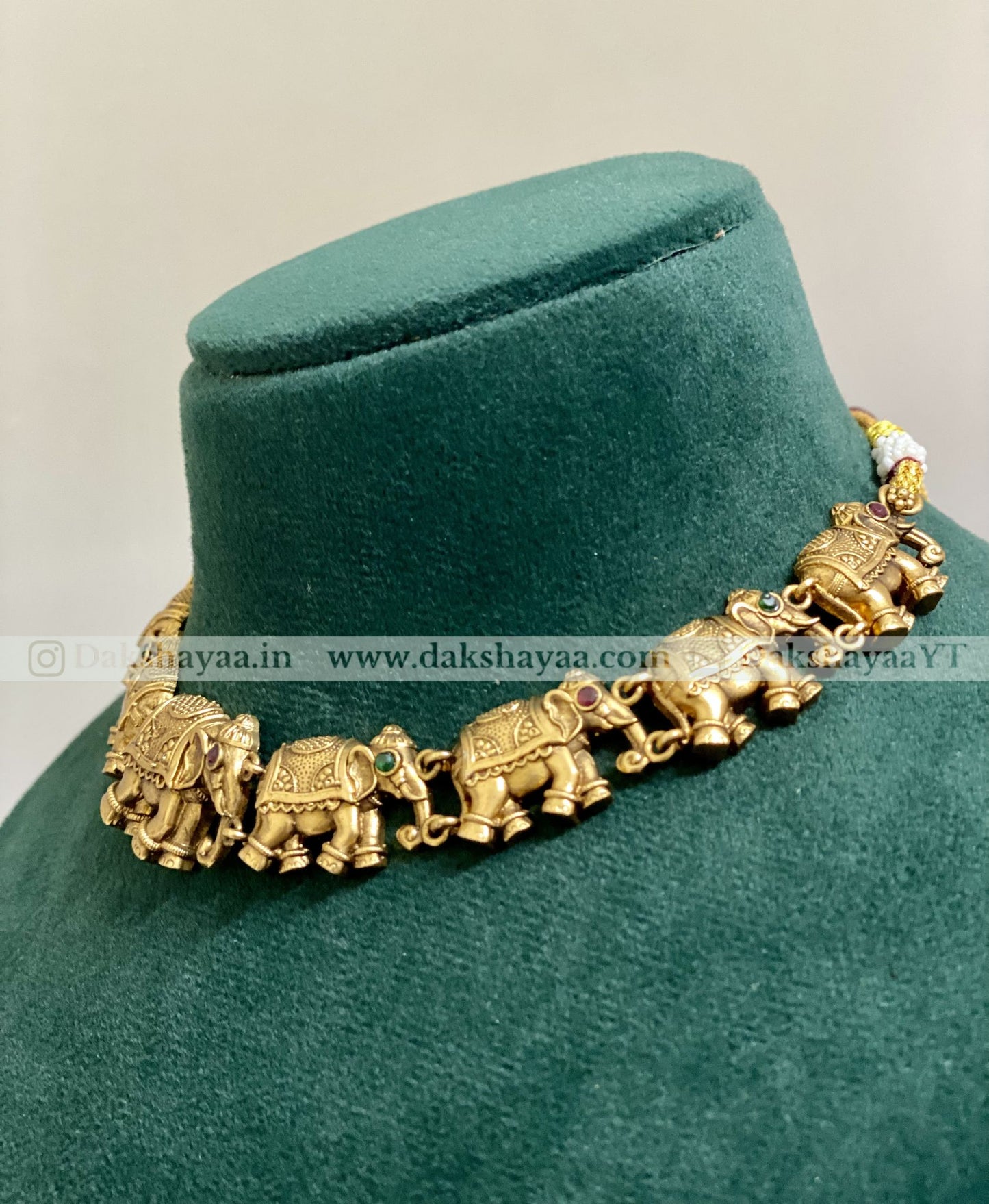 Gold elephant necklace on a green velvet stand with visible brand name.
