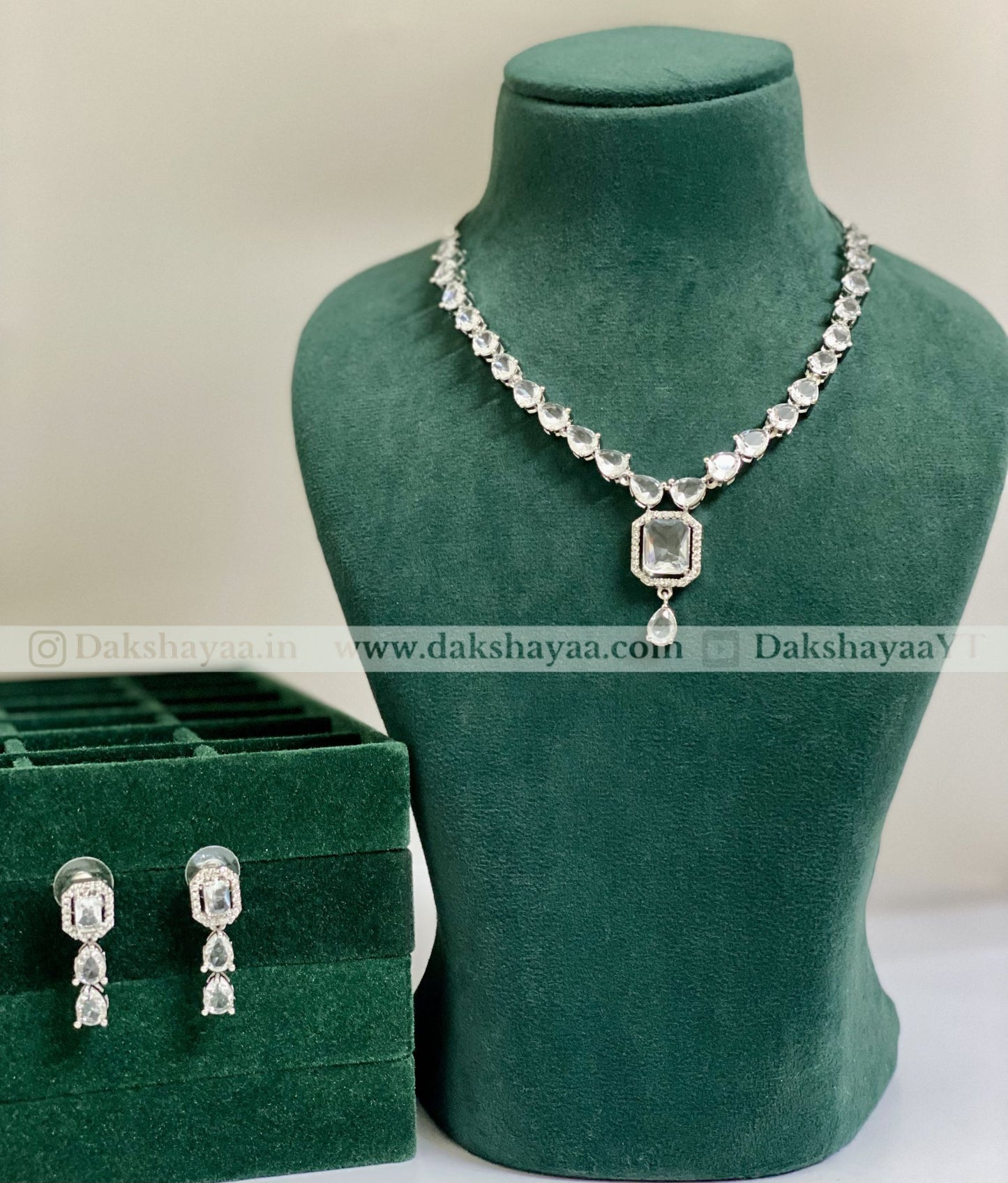 Jewelry set with necklace and earrings on a green mannequin and box, brand 'Dakshayaa' visible.