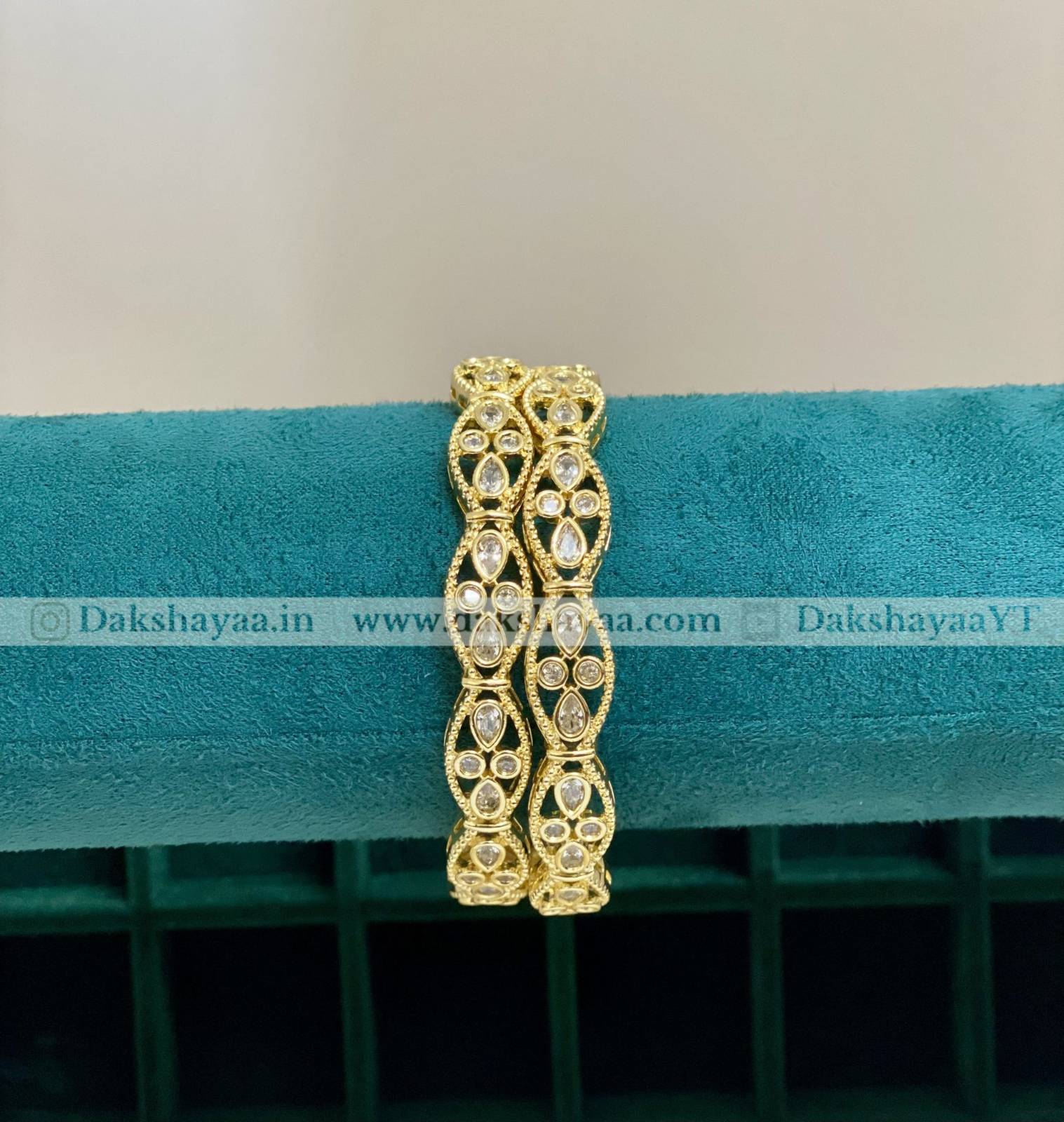 Gold bracelet with intricate design on a teal cushion