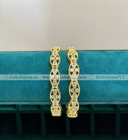Gold hoop bangles on a teal cushion with 'Dakshayaa.in' branding.