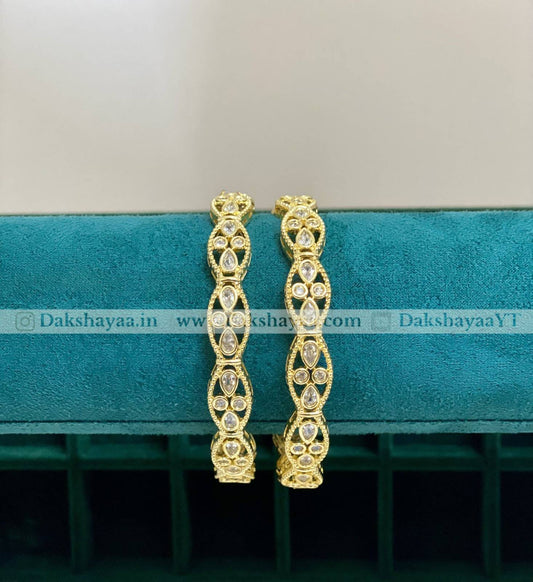 Gold hoop bangles on a teal cushion with 'Dakshayaa.in' branding.