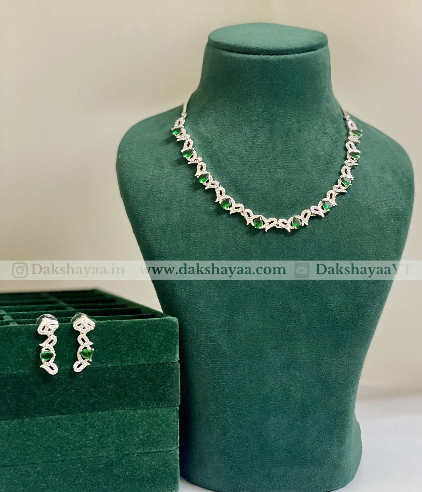 Necklace and earrings on a green mannequin with a green box, branded 'Dakshayaa'.