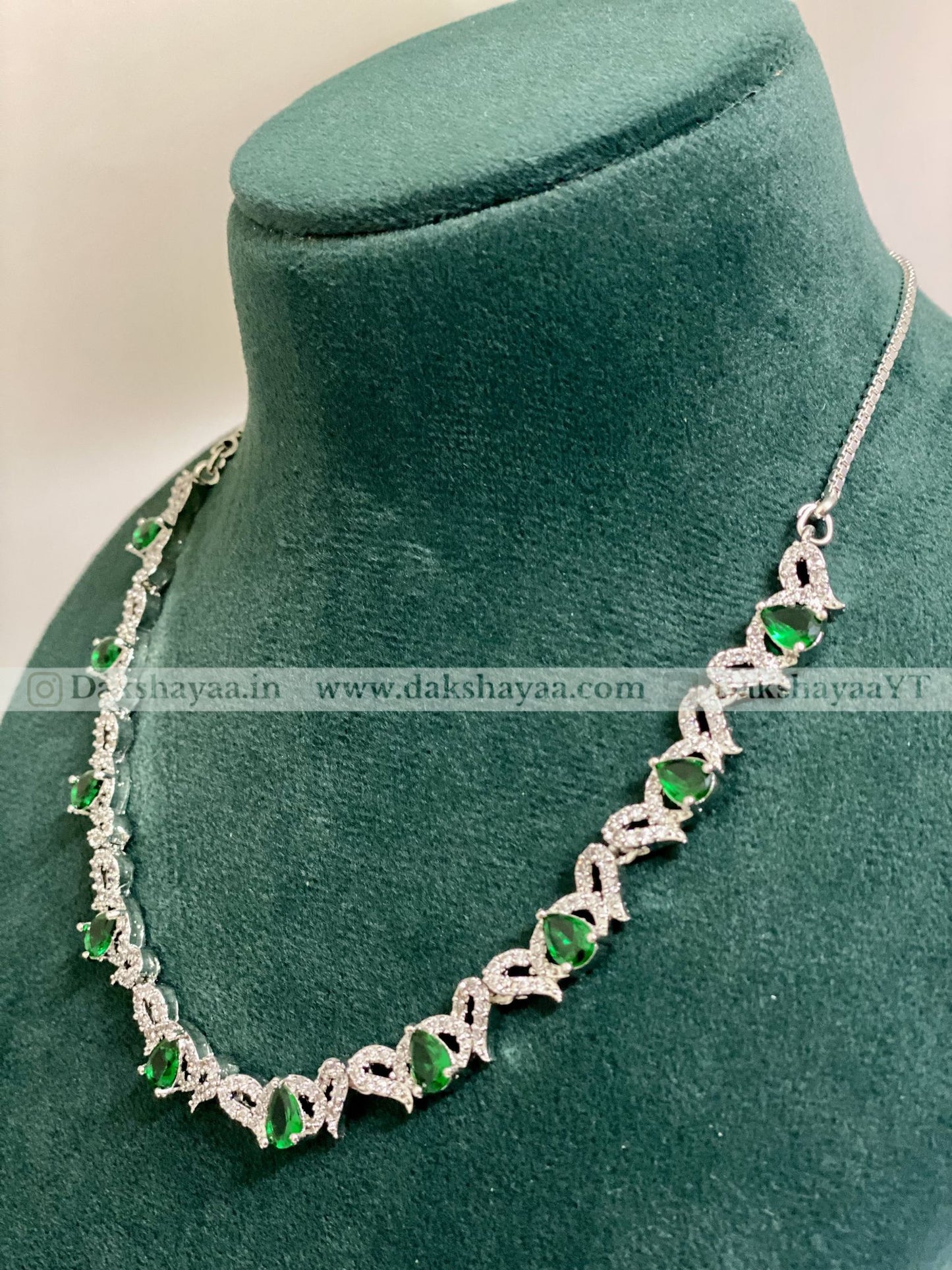 Silver necklace with green gemstones on a green velvet stand