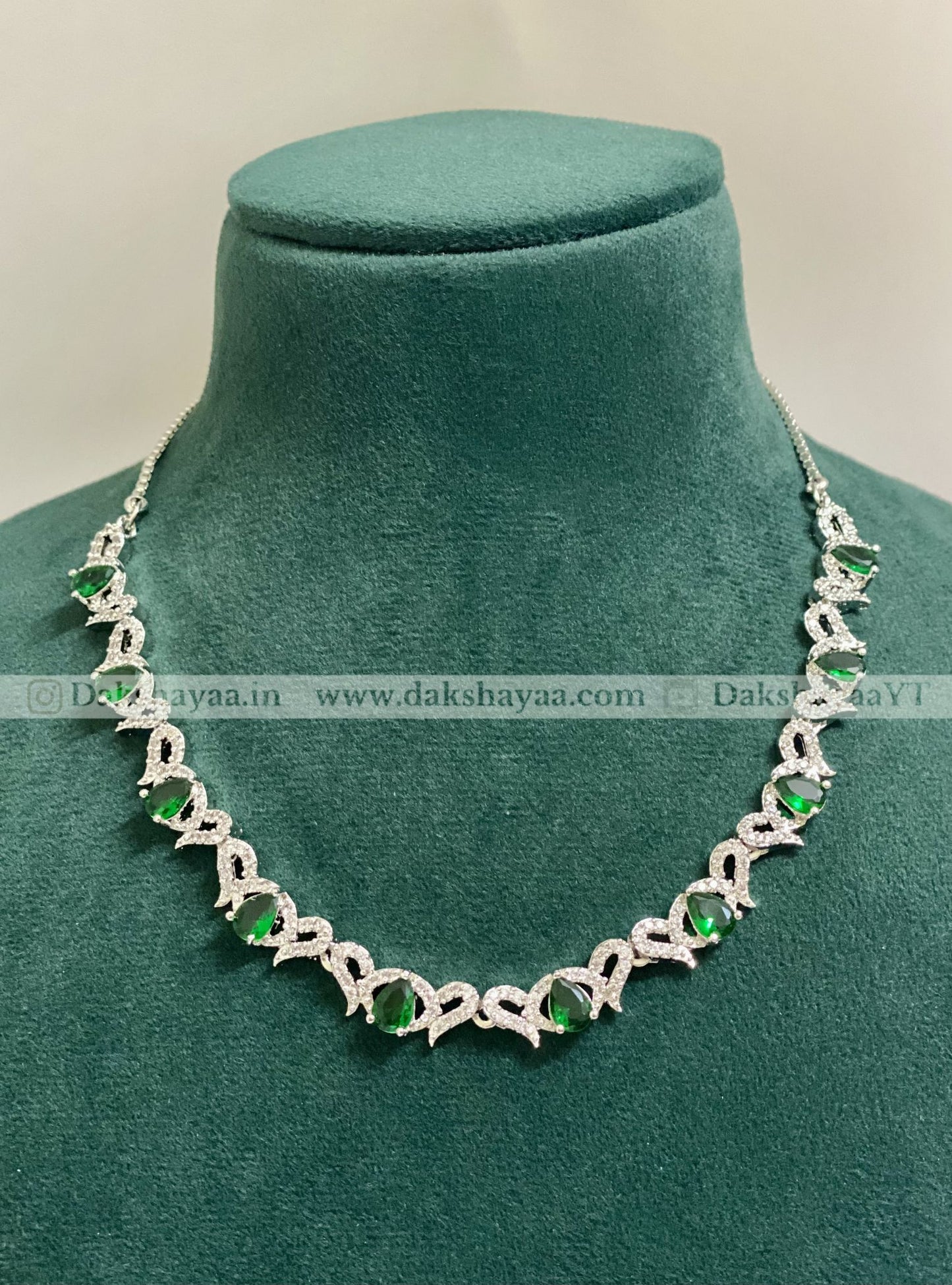 Silver necklace with green gemstones on a green velvet stand