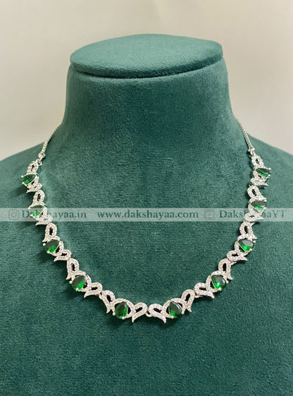 Silver necklace with green gemstones on a green velvet stand