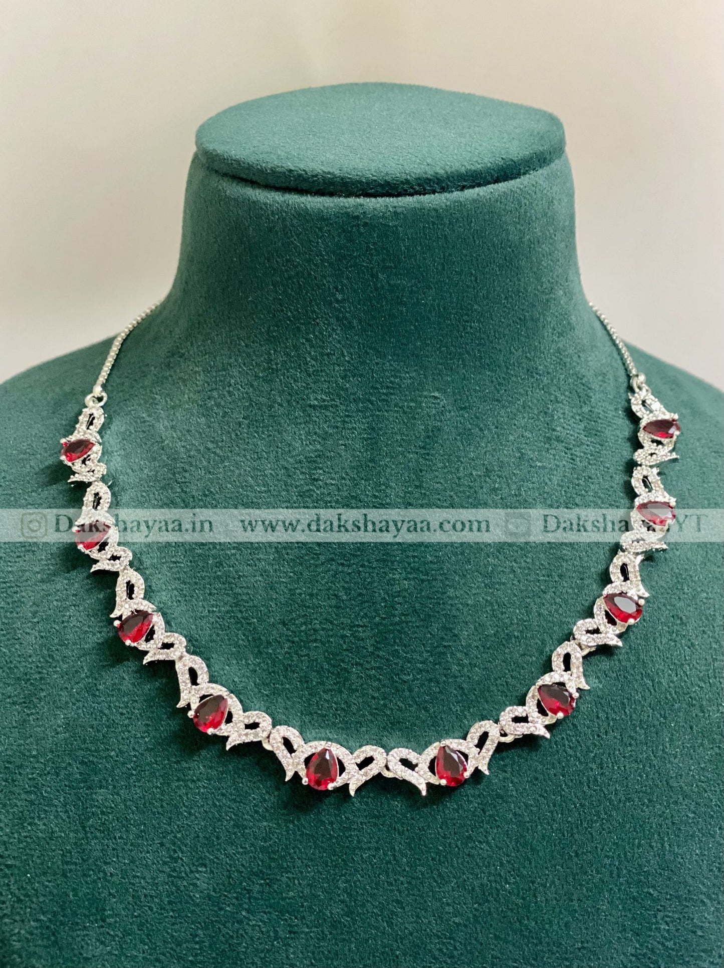 Silver necklace with red stones on a green velvet mannequin