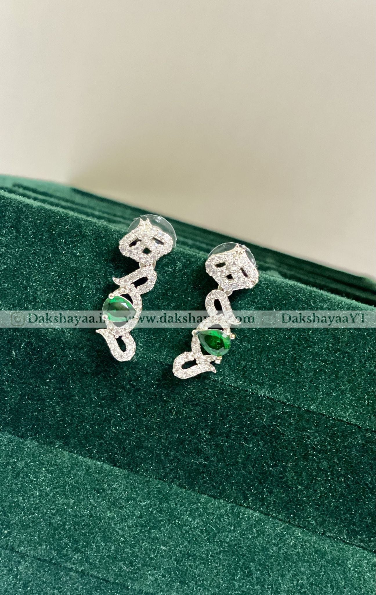 Silver earrings with green gemstones on a green velvet surface