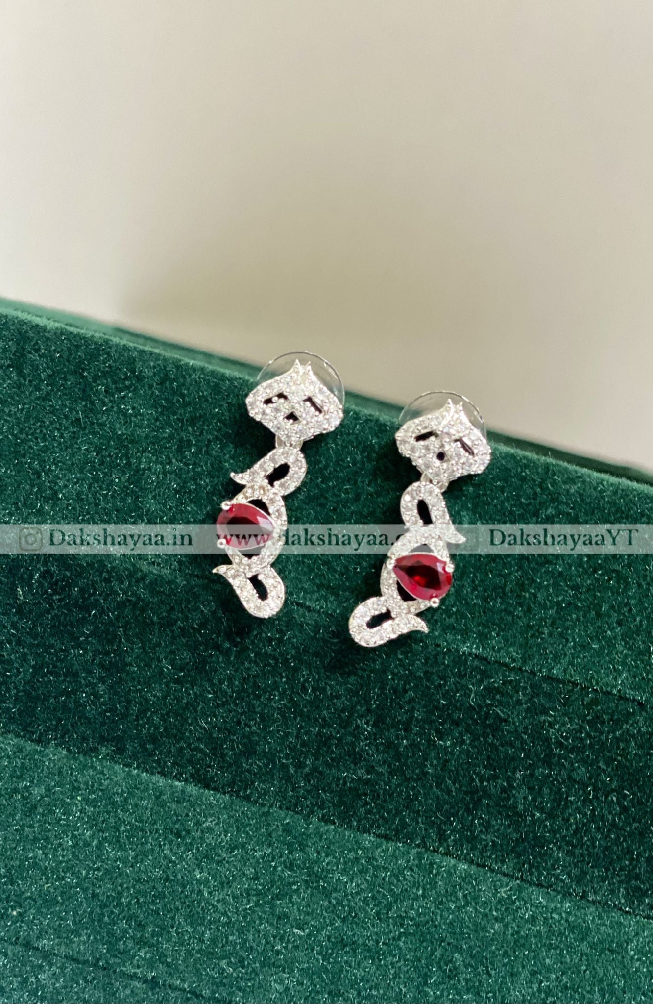 Silver earrings with red gemstones on a green cushion