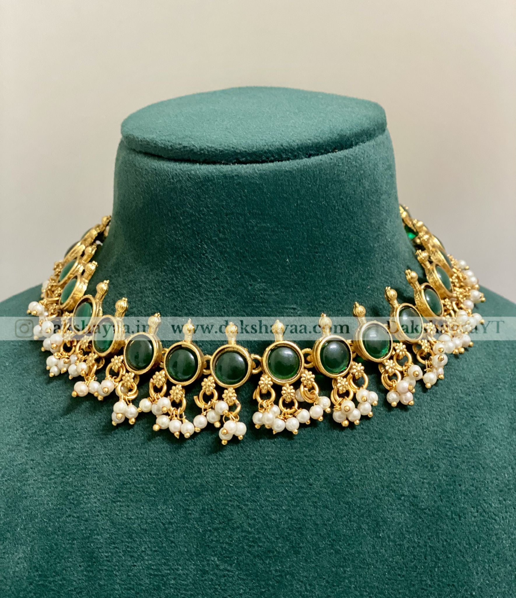 Ornate necklace with green stones and pearls on a green velvet stand