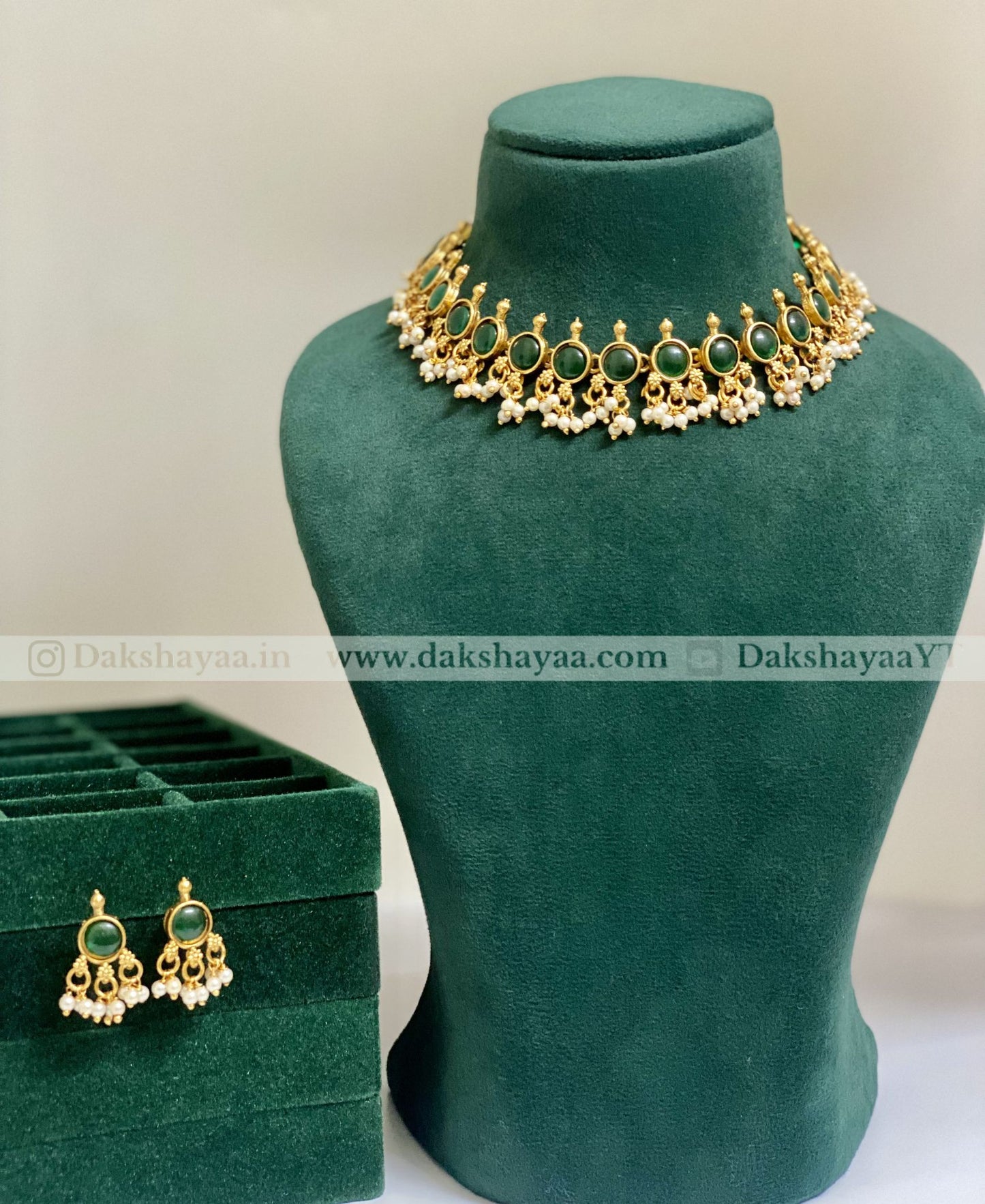 Gold necklace with green stones on a green velvet stand, accompanied by matching earrings in a green box.