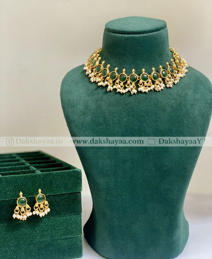 Gold necklace with green stones on a green velvet stand, accompanied by matching earrings in a green box.