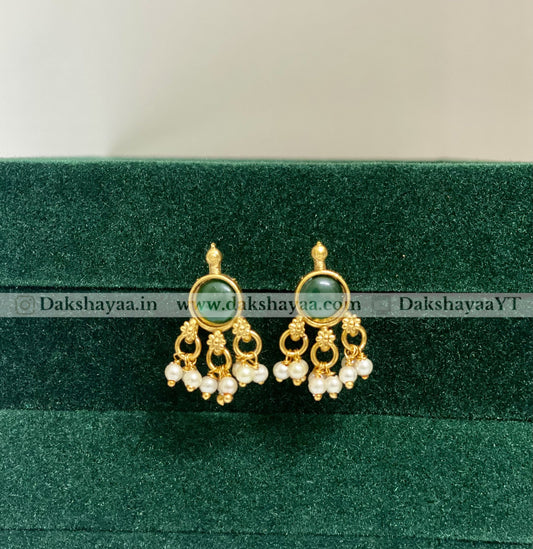 Gold earrings with green gemstone and pearl drops on a green velvet background