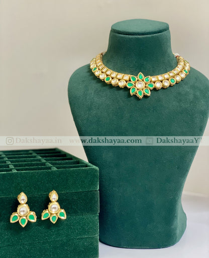 Gold necklace with green stones on a green mannequin bust, next to a matching earring set and green jewelry box.