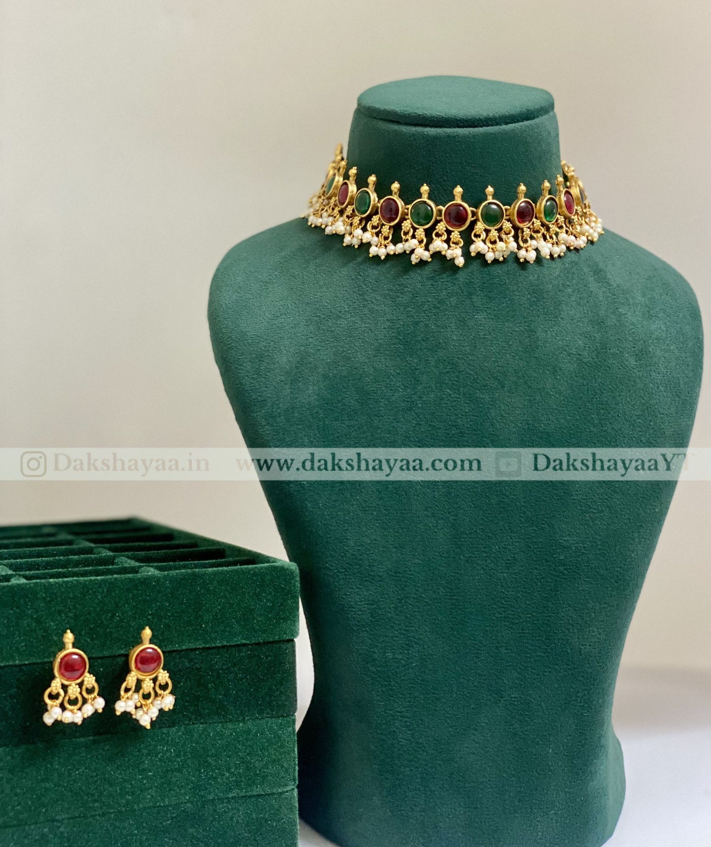 Gold necklace with red and green stones on a green mannequin bust, with matching earrings below.