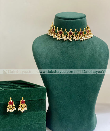 Gold necklace with red and green stones on a green mannequin bust, with matching earrings below.