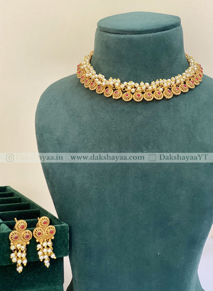 Gold necklace and earrings on a green velvet stand with 'Dakshayaa' branding.