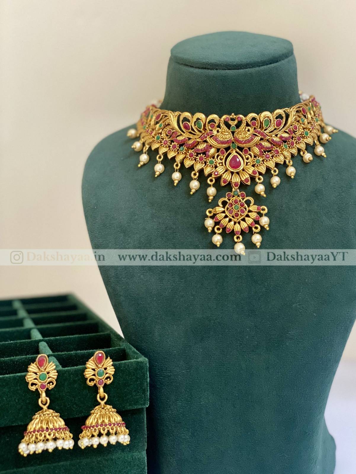 Gold necklace and earrings on a green mannequin with visible branding.