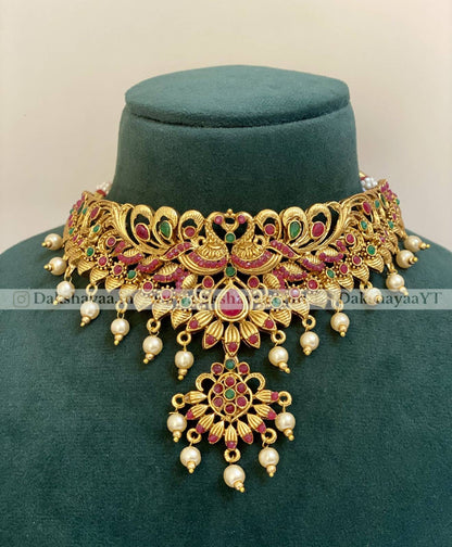 Ornate gold necklace with red and green stones on a green velvet stand