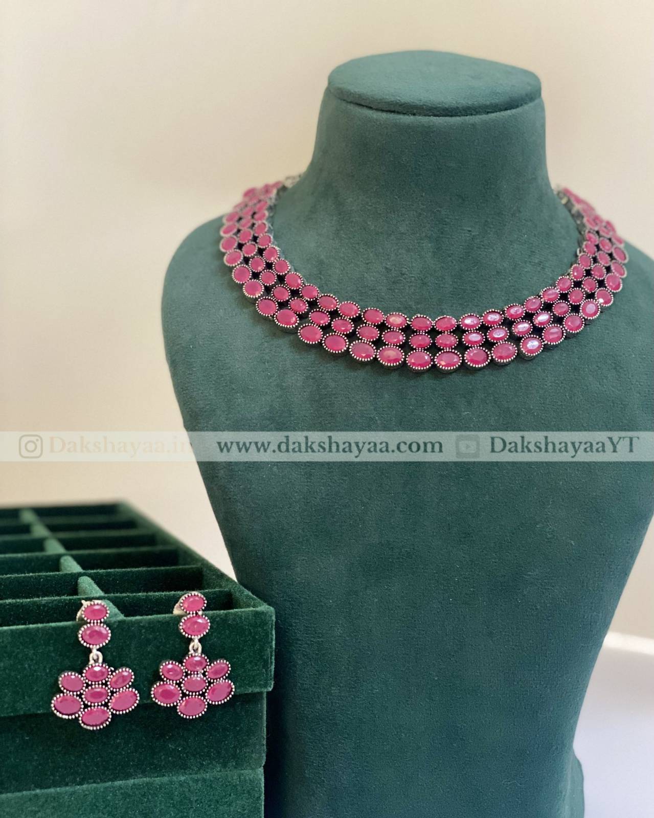Pink necklace and earrings on a green mannequin with a visible brand logo.
