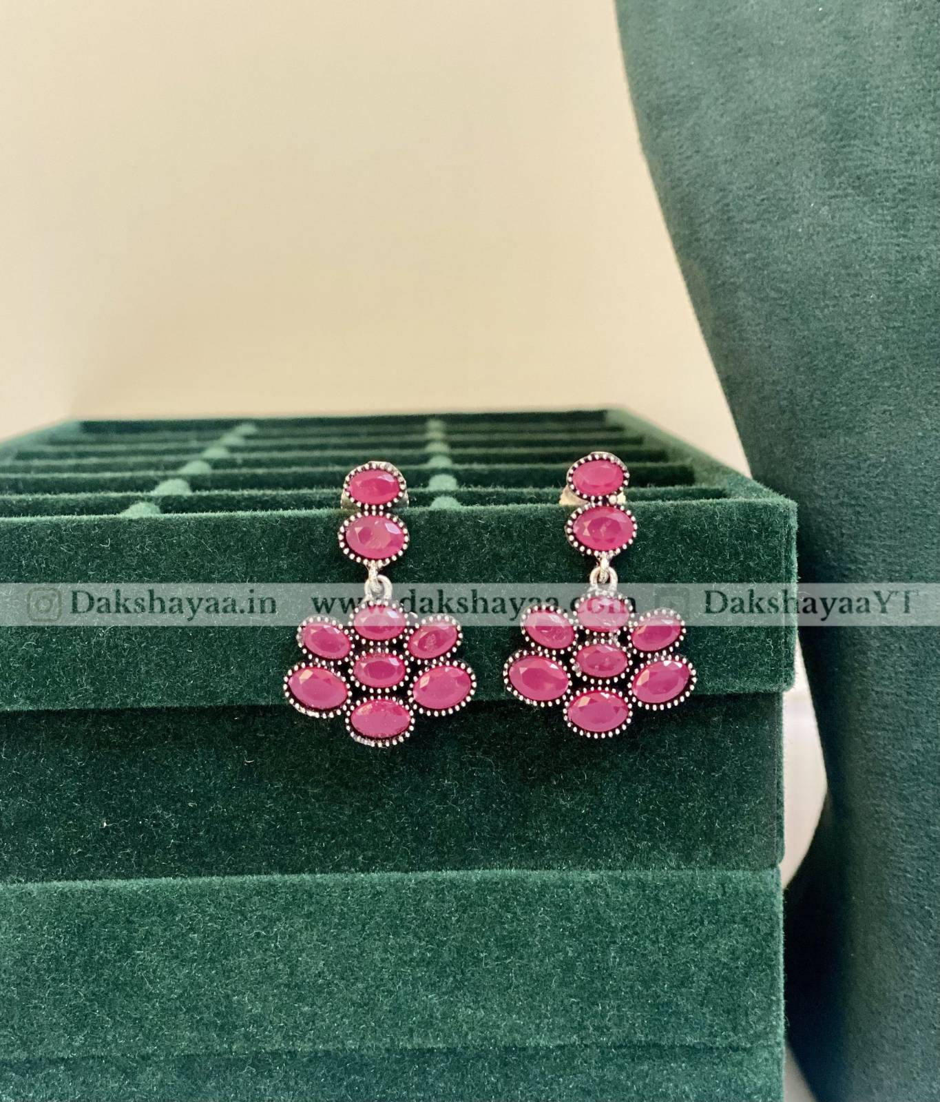 Pink earrings on a green jewelry display box with visible branding.