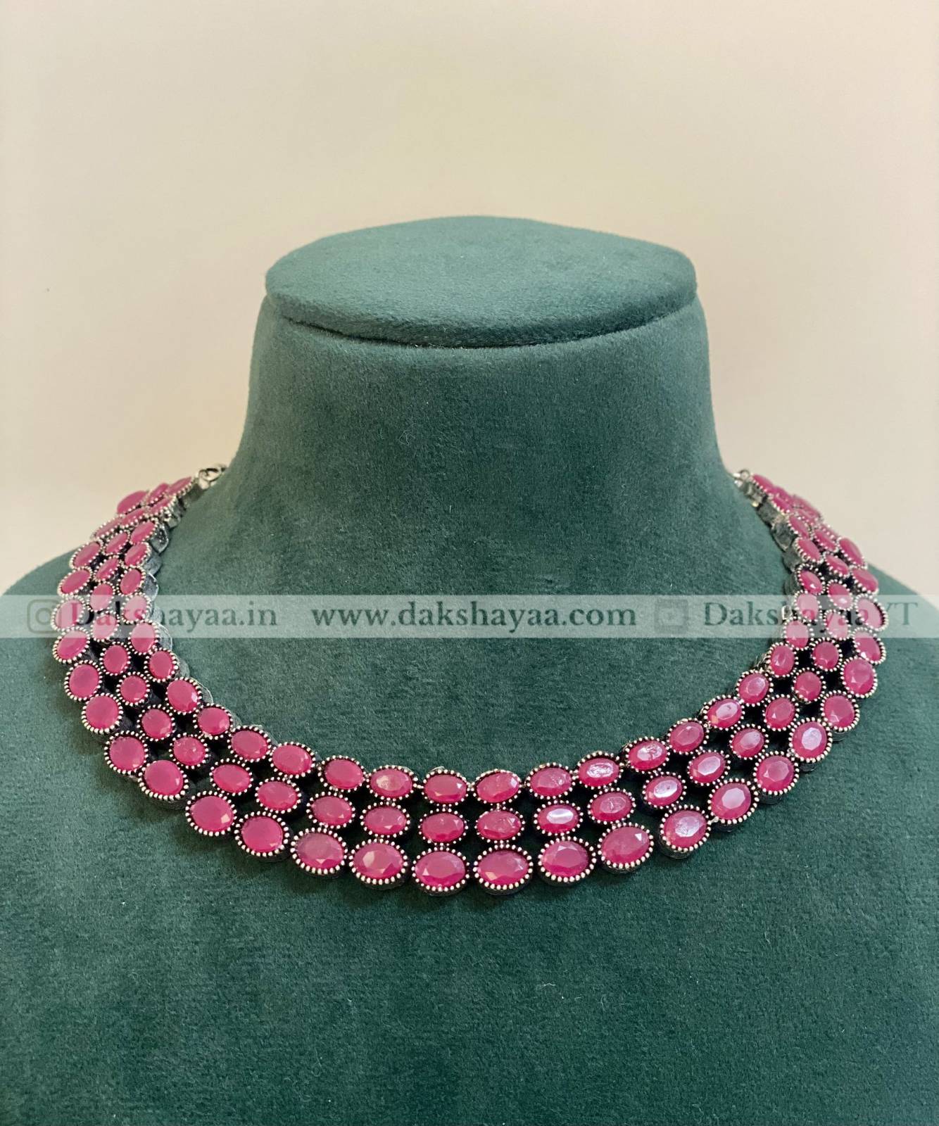 Pink beaded necklace on a green mannequin against a beige background