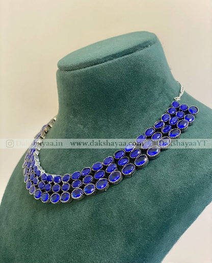 Blue necklace on a green velvet stand with visible branding.