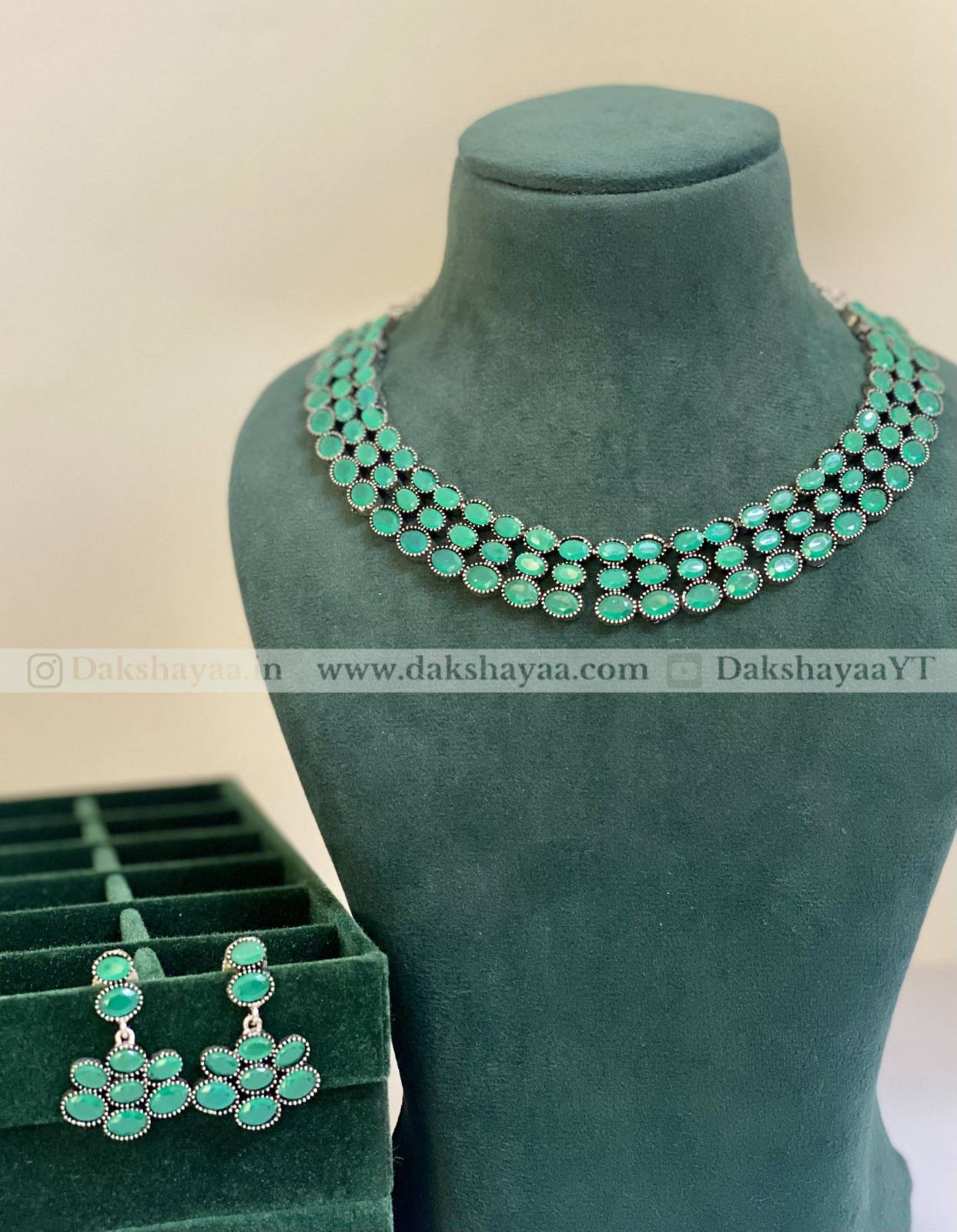 Green necklace and earrings on a mannequin with a branded background